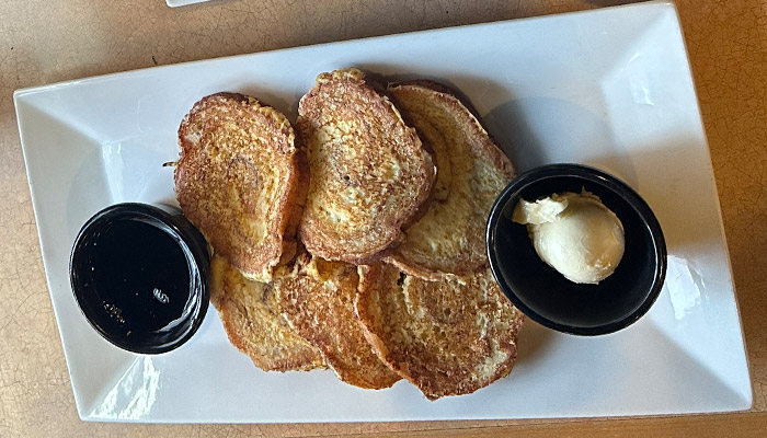 Five slices of French toast from the Matera Italian Breakfast Menu with syrup and a side of butter.